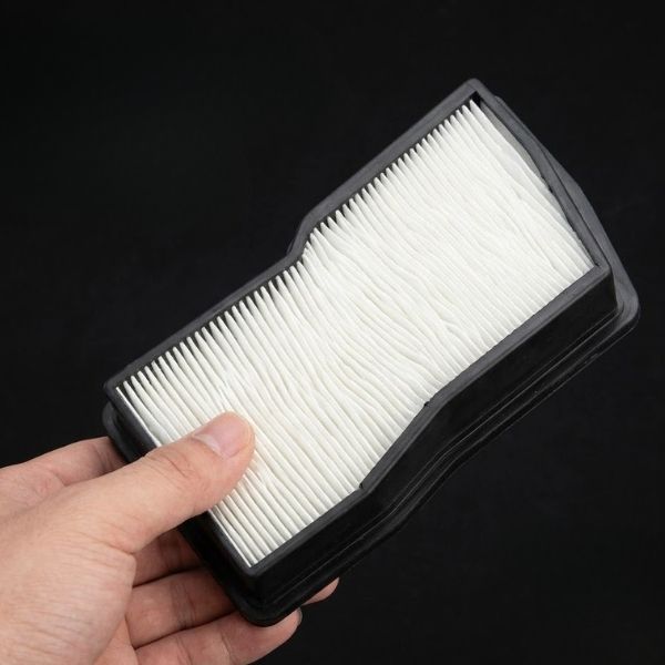 A close-up view of a hand holding a new, clean white air filter.