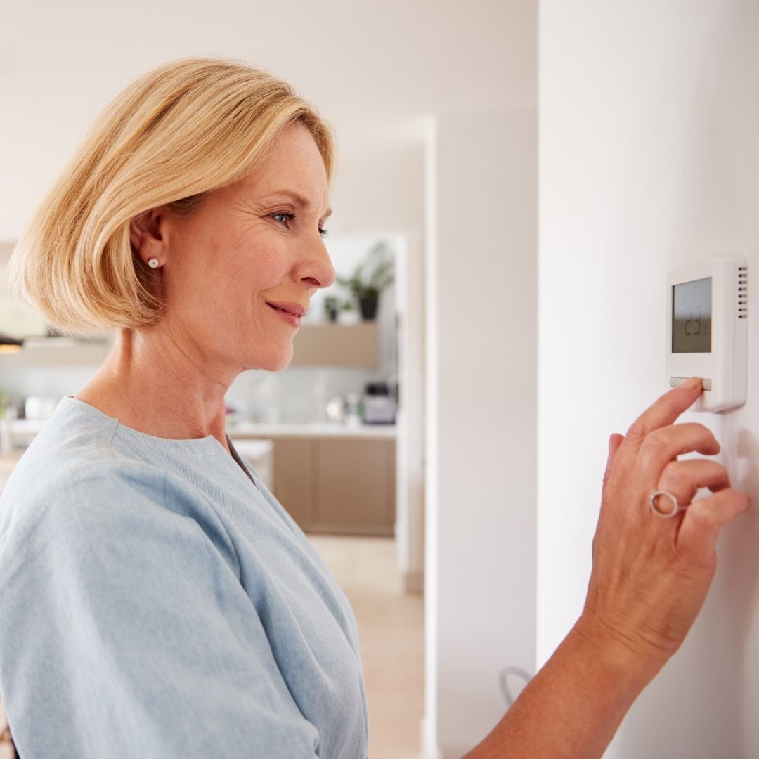 A woman adjusting the thermostat in her home.